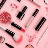 Various cosmetic accessories for makeup and manicure on trendy pastel pink background with red flowers. Blush, brush, eye shadow, mascara, perfume, lipstick, nail Polish. Skin care products.